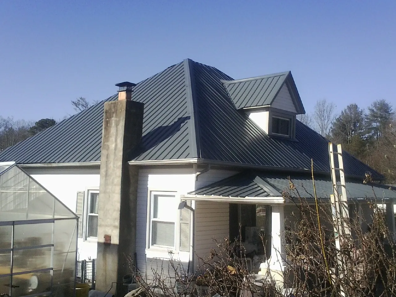 Dark blue standing seam metal roof on a white farmhouse with dormer — Slate & Tile Roof Repair by Roofing Brothers in Glenview