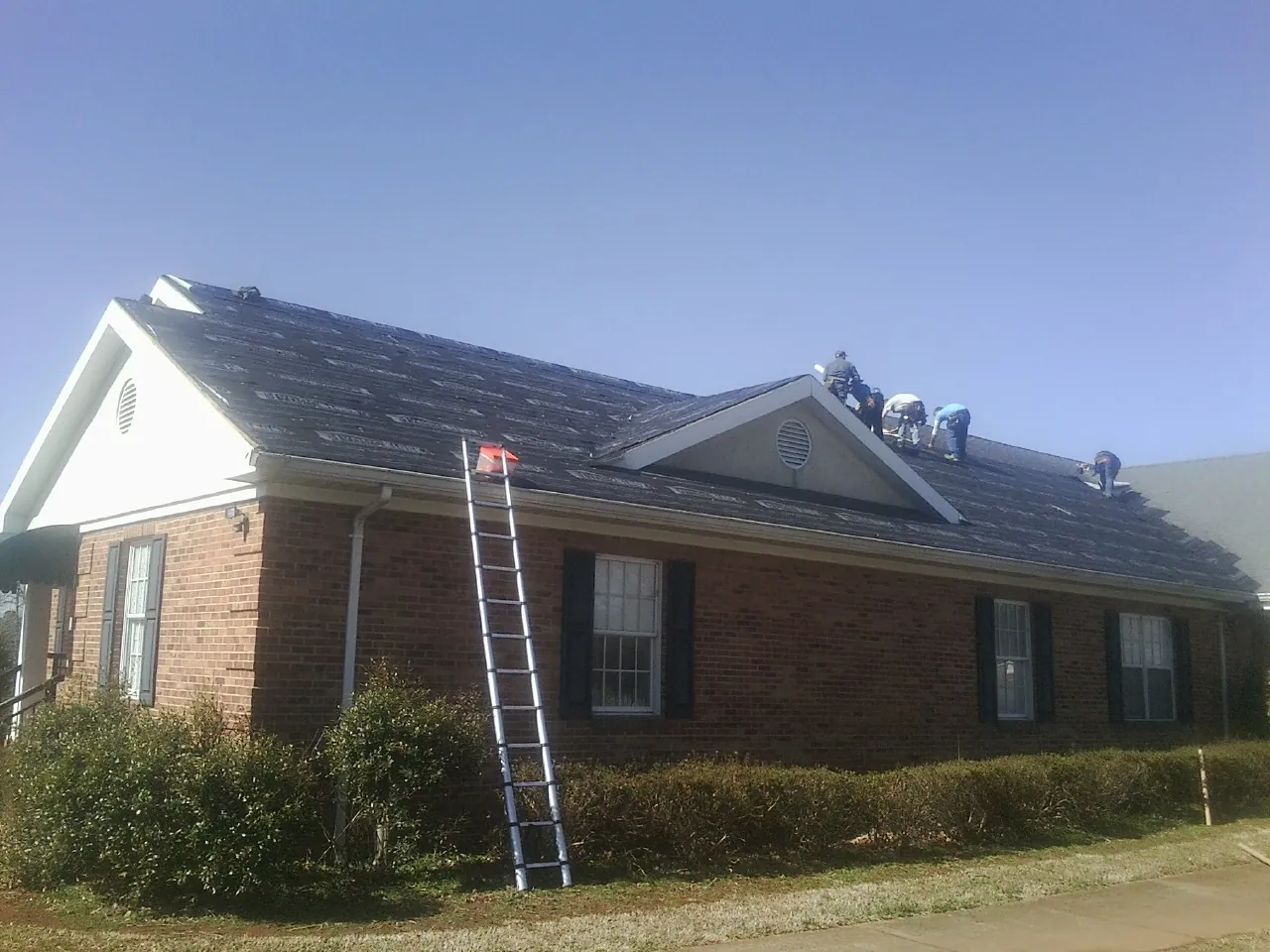 Crew tearing shingles off a brick ranch roof with a ladder set — Emergency Roof Repair work by our crew in Glenview