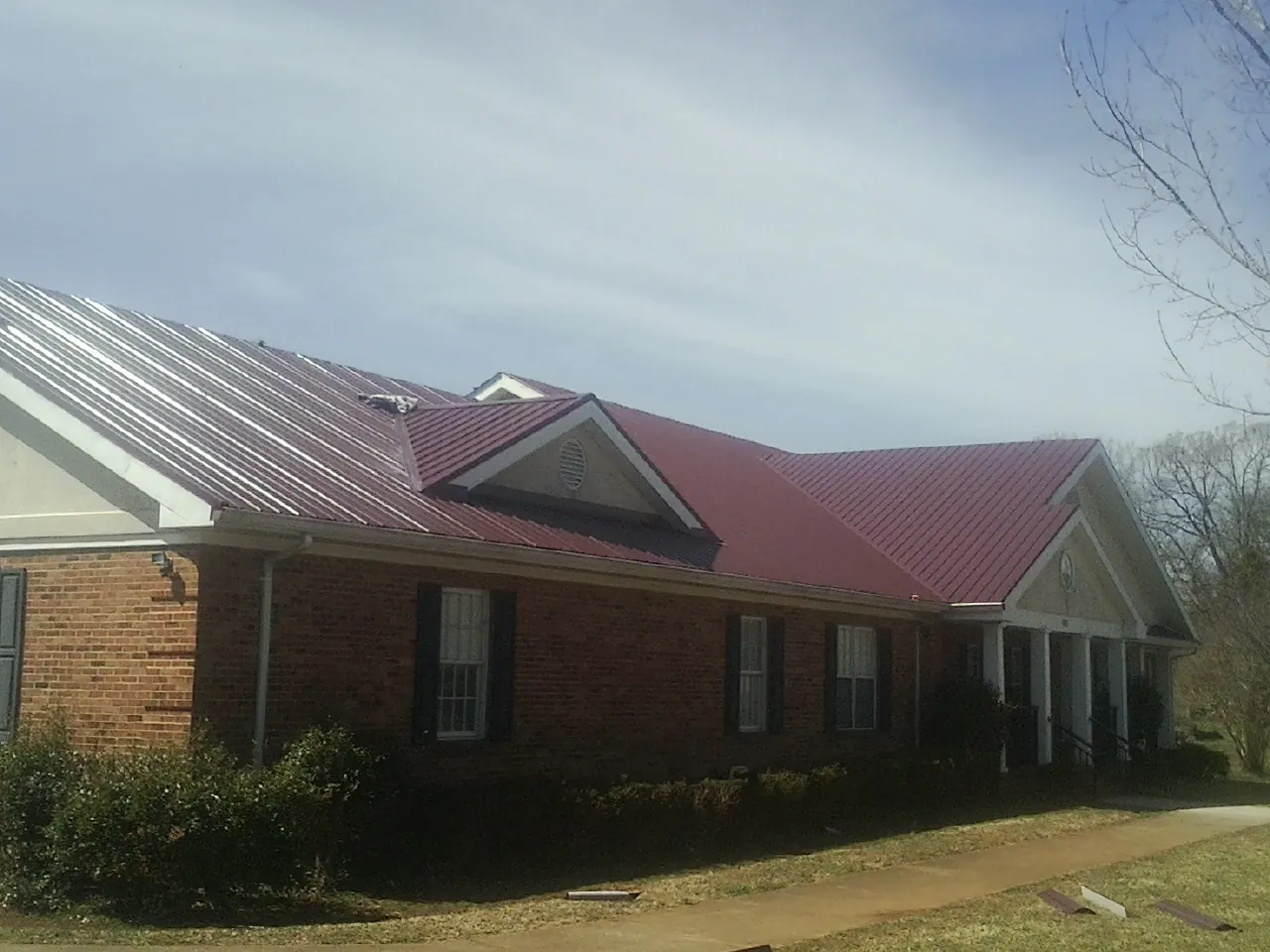 Red metal roof with gabled entries on a long brick building, from a Hail Damage Roof Repair job in Glenview