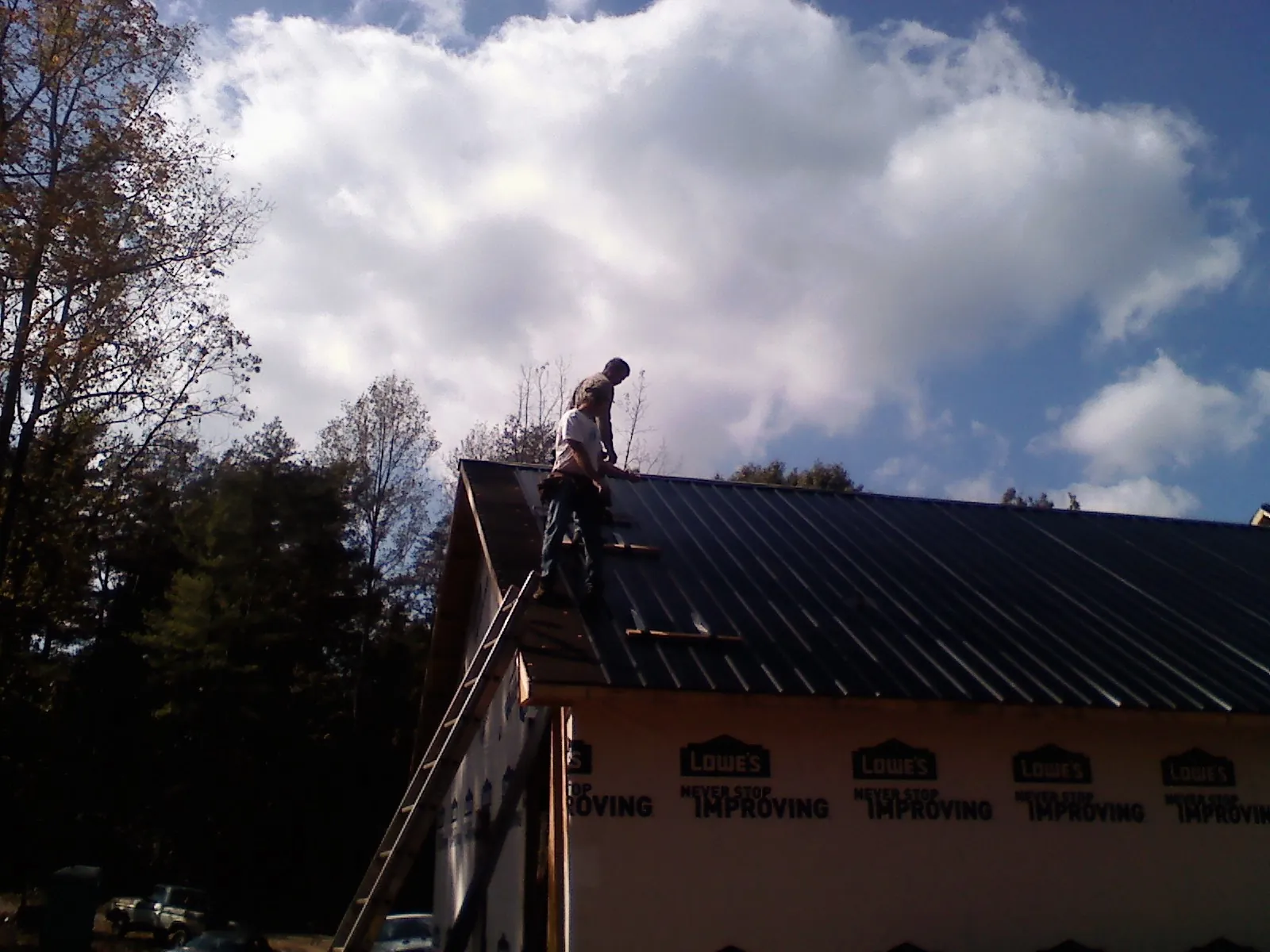Roofer fastening dark metal panels high against a cloudy sky, from a Roof Inspection job in Glenview