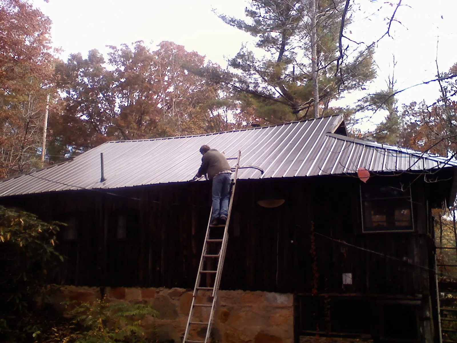 Roofer on a ladder working along the edge of a cabin metal roof in Glenview
