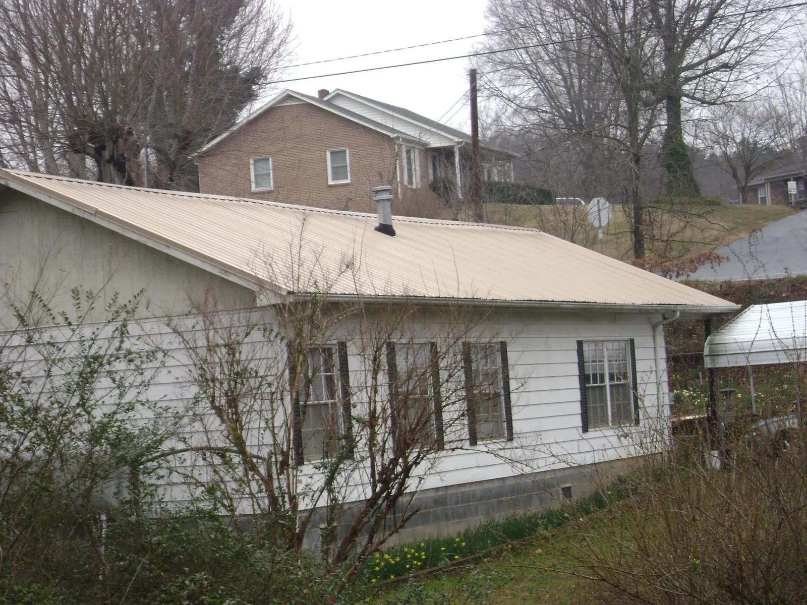 Tan metal roof on a white sided house set into a hillside — Commercial Roofing by Roofing Brothers in Glenview